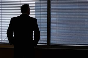 Symboldbild: Mann vor einem mit Jalousie fast verschlossenen Fenster, der einen Geldwäschevorfall beobachtet, aufdeckt und meldet