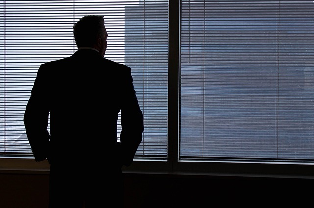 Symboldbild: Mann vor einem mit Jalousie fast verschlossenen Fenster, der einen Geldwäschevorfall beobachtet, aufdeckt und meldet