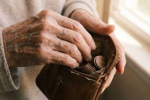 Symbolbild: Hände eines älteren Menschen mit einer Geldbörse voller Münzen symbolisieren Pensionsrückstellungen